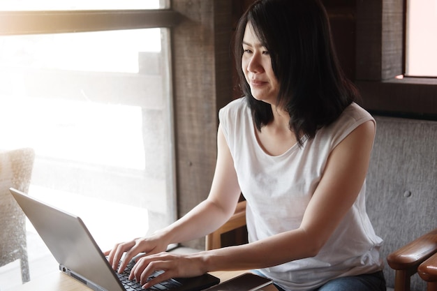 Uma jovem asiática sorridente está online trabalhando ou fazendo compras com laptop no escritório