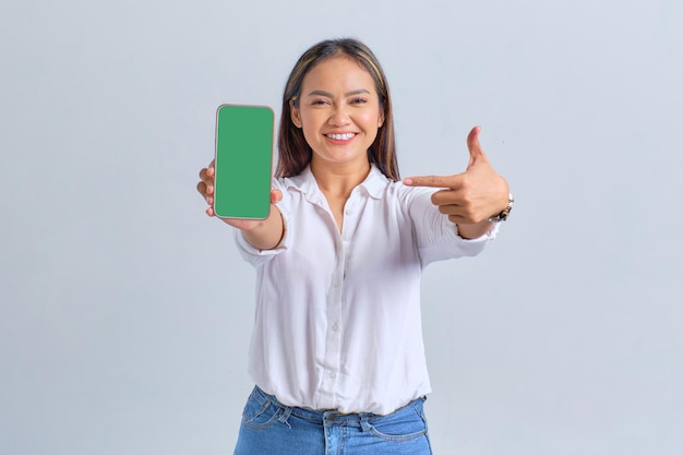 Uma jovem asiática sorridente mostrando um celular de tela em branco recomendando aplicativo móvel isolado sobre fundo branco