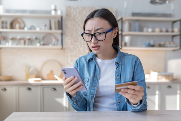 Uma jovem asiática tenta fazer uma operação bancária usa um telefone e um cartão de crédito bancário decepcionado e insatisfeito com o resultado