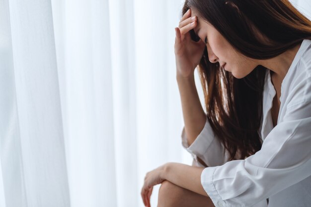 Uma jovem asiática triste e estressada, sentada sozinha no quarto