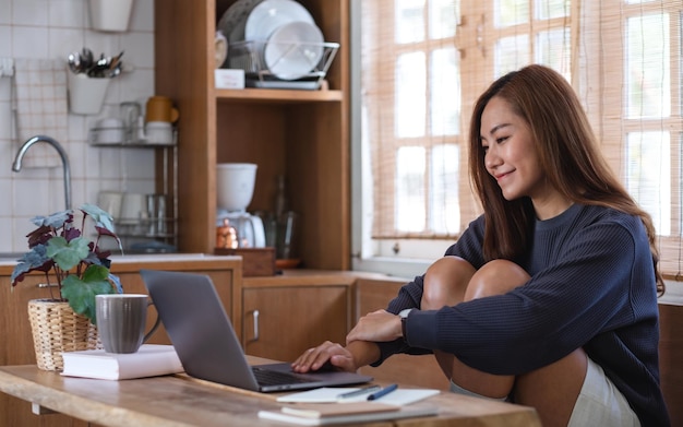 Uma jovem asiática usando e trabalhando no laptop em casa