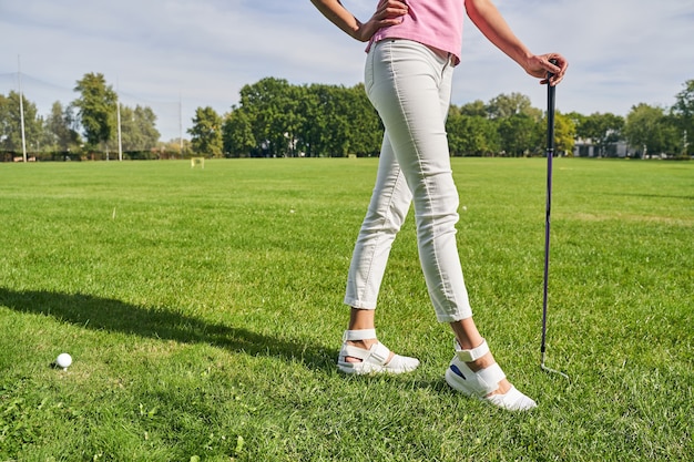 Uma jovem atleta esguia apoiando uma das mãos em um taco de golfe