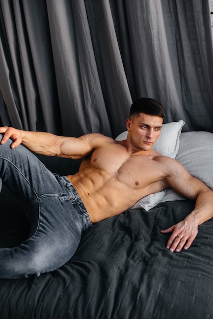 Uma jovem atleta sexy com abdominais perfeitos está deitada na cama do estúdio em jeans