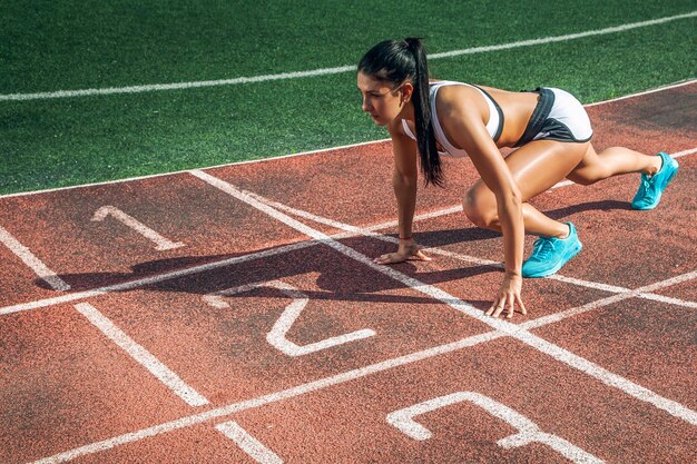 Uma jovem atlética está em um início baixo para correr no estádio em um dia de verão