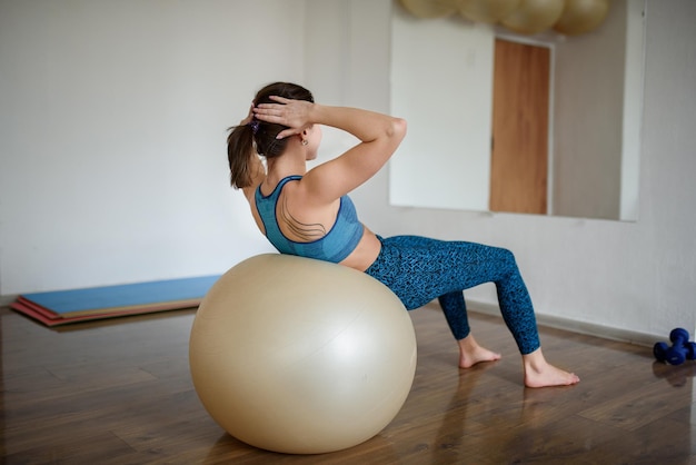 Uma jovem atlética treina seu abdômen em uma bola de fitness no ginásio vista traseira