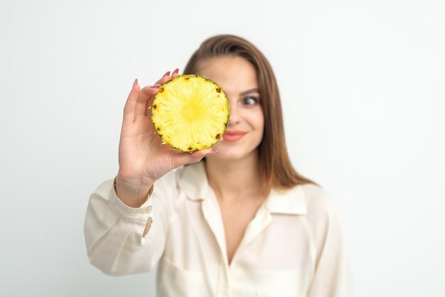 Uma jovem atraente bonita caucasiana sorridente mulher segura uma fatia de abacaxi cobrindo o olho dela contra um fundo branco. Conceito de alimentação saudável.