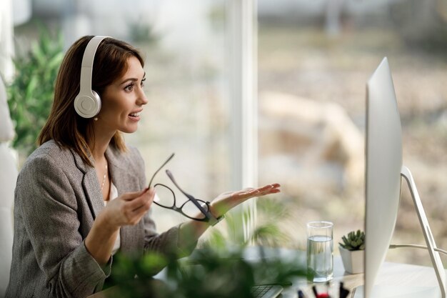 Uma jovem atraente com fones de ouvido trabalhando no computador no escritório em casa.