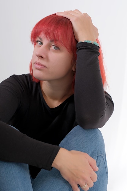 Uma jovem atraente com um penteado curto laranja em uma camiseta preta e jeans posando no estúdio em um fundo branco