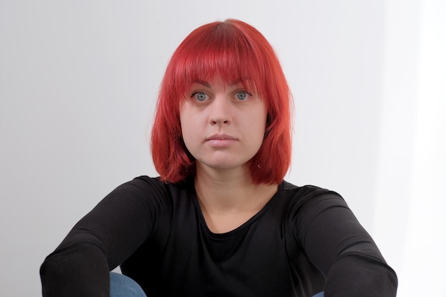 Uma jovem atraente com um penteado curto laranja em uma camiseta preta e jeans posando no estúdio em um fundo branco