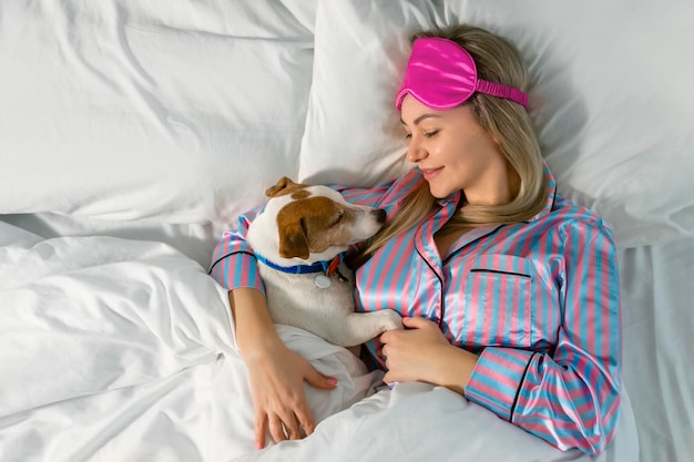 Uma jovem atraente de pijama está segurando um cachorro enquanto está deitada na cama