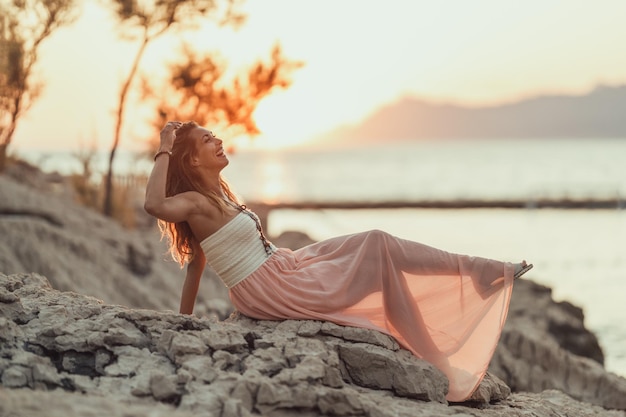 Uma jovem atraente de vestido está se divertindo e apreciando o pôr do sol de verão à beira-mar maravilhosa.