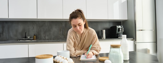 Foto uma jovem atraente e alegre assando na cozinha fazendo massa segurando um livro de receitas com ideias
