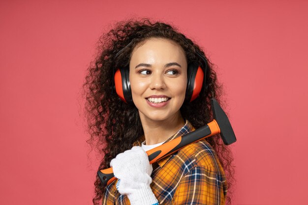 Foto uma jovem atraente em fones de ouvido de construção e com um martelo nas mãos