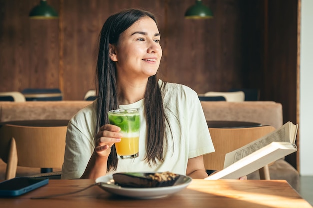 Uma jovem atraente em um café está lendo um livro com um copo de limonada