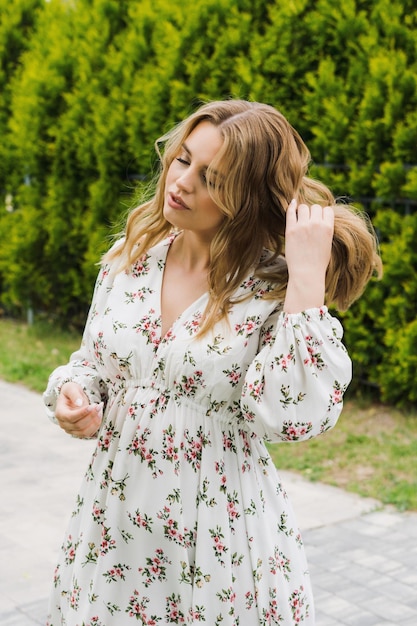 Uma jovem atraente em um vestido de verão posa contra um fundo de vegetação