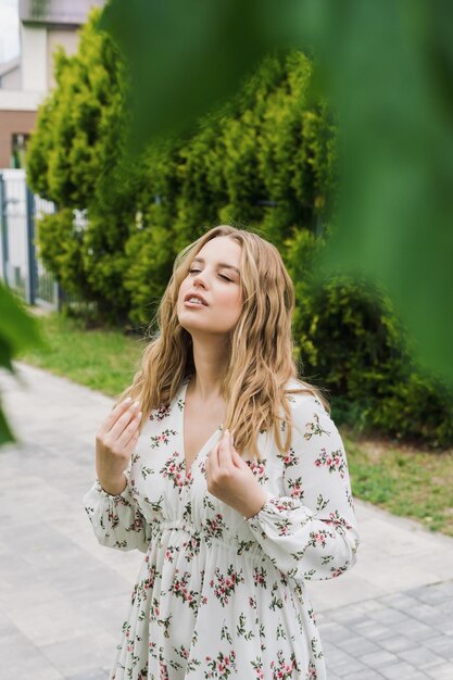 Uma jovem atraente em um vestido de verão posa contra um fundo de vegetação