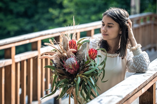 Uma jovem atraente em uma ponte de madeira está com um buquê de flores exóticas.