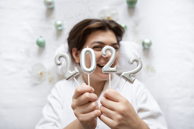 Uma jovem atraente encontra-se com uma túnica branca para um procedimento de spa, segura os números 2022 sobre um fundo branco, o conceito de Natal e Ano Novo.