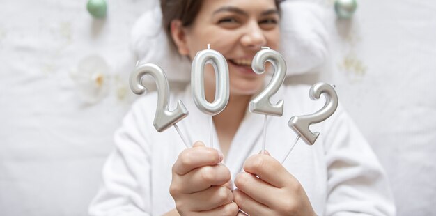 Uma jovem atraente encontra-se com uma túnica branca para um procedimento de spa, segura os números 2022 sobre um fundo branco, o conceito de Natal e Ano Novo.