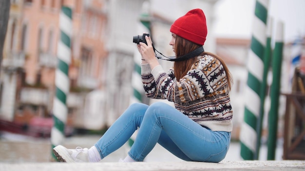 Uma jovem atraente senta-se à beira-mar e tira uma foto das ruas de veneza