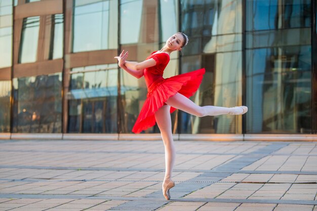 Uma jovem bailarina com um tutu vermelho brilhante dançando no cenário de uma cidade