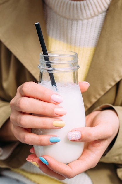 Uma jovem bebe um milkshake ao ar livre em uma jarra de vidro elegante com um canudo