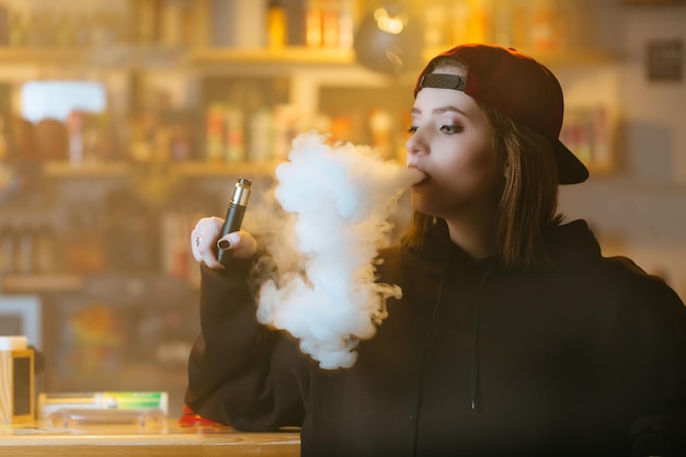 Uma jovem bonita de boné vermelho fuma um cigarro eletrônico no estilo hiphop da loja vape