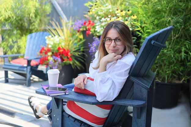 Uma jovem bonita descansa no café ao ar livre olhando para as flores da câmera em um pano de fundo