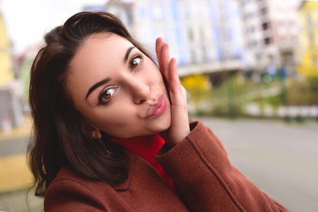 Foto uma jovem bonita e elegante com um casaco castanho de outono tira uma selfie na rua para o seu namorado