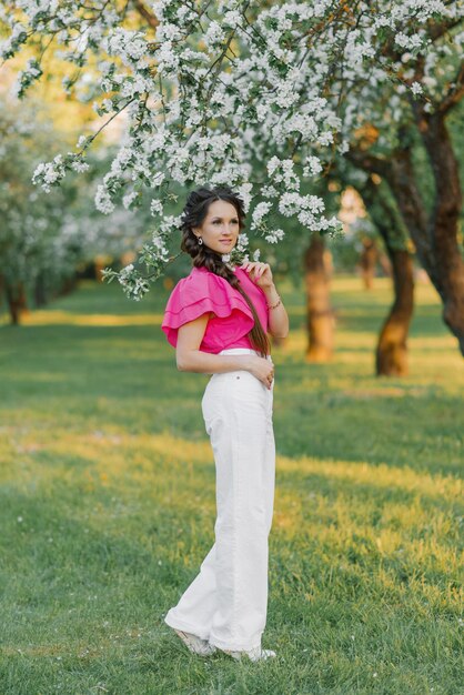 Uma jovem bonita em calças brancas e uma blusa rosa brilhante passeia por um parque de primavera