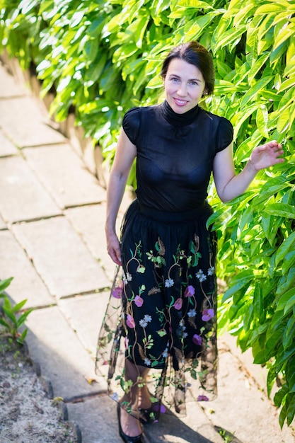 Uma jovem bonita em roupas pretas em pé perto de um arbusto em um quintal