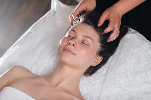 Uma jovem bonita está desfrutando de uma massagem profissional na cabeça no spa. Cuidado do corpo. Salão de beleza.