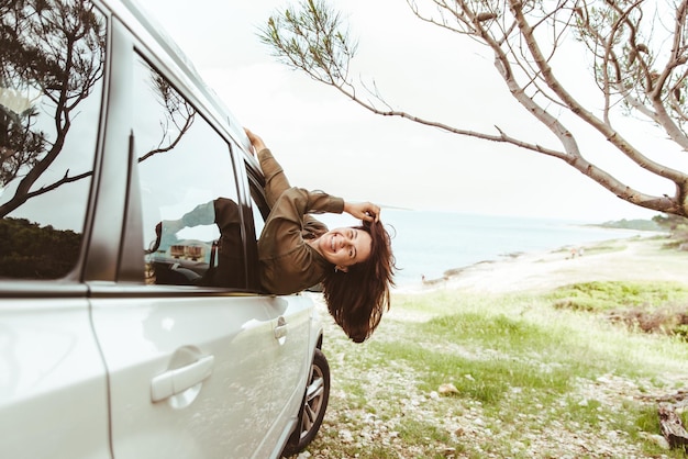 Foto uma jovem bonita sai da janela do carro na praia do mar nas férias de verão de fundo