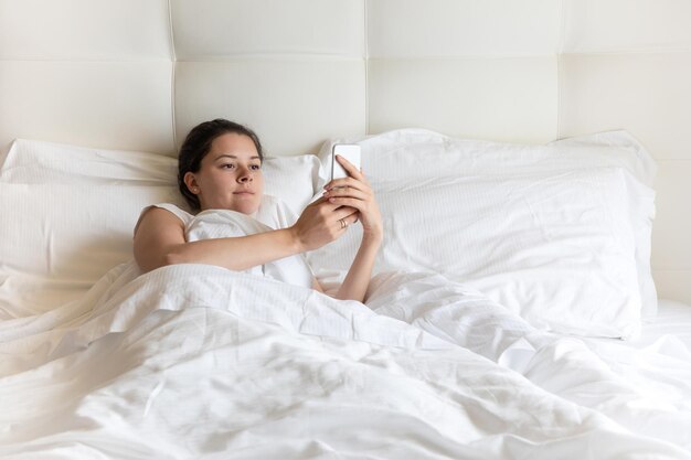 Uma jovem bonita usando um telefone celular enquanto está deitada na cama em casa