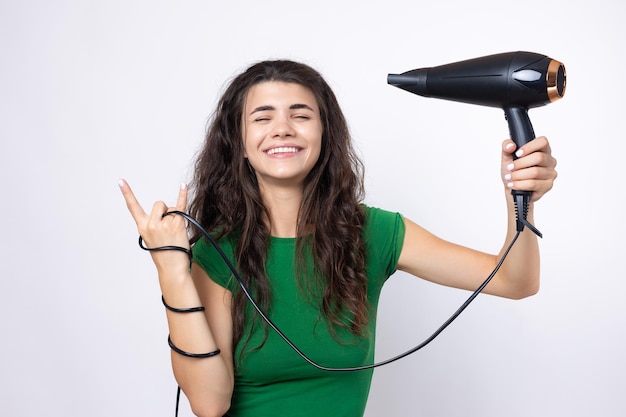 Uma jovem bonita vestida com um top verde seca seu lindo cabelo longo e sedoso com um secador de cabelo