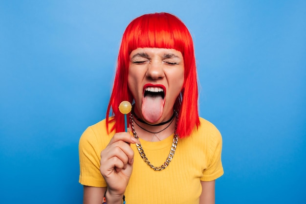 Uma jovem brilhante e engraçada com cabelo vermelho lambe um pirulito Studio imagem colorida de uma mulher estilo pinup com um pirulito em uma vara em um fundo azul
