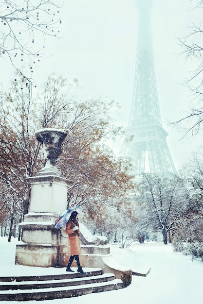 Uma jovem caminha em um inverno nevado paris contra a torre eiffel