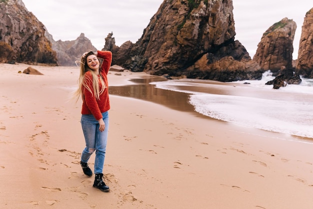 Uma jovem caminha na areia na praia com grandes rochas ao fundo