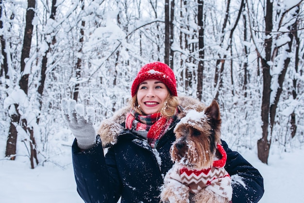 Uma jovem caminha na floresta inferior no inverno com um cachorro vestindo um suéter de natal