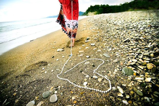 Uma jovem caminha na praia na areia são contas em forma de coração