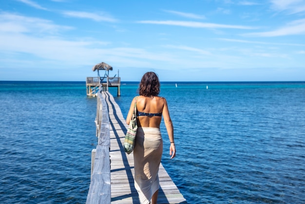 Uma jovem caminhando ao longo de uma passarela de madeira ao longo da praia de sandy bay, em roatan island. honduras