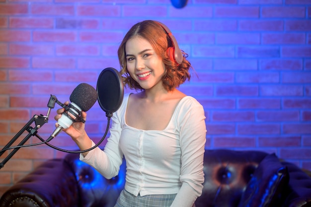 Uma jovem cantora sorridente usando fones de ouvido com um microfone enquanto grava música em um estúdio de música com luzes coloridas.