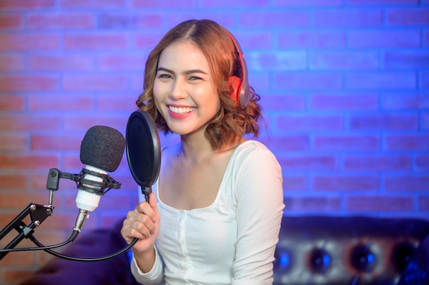 Uma jovem cantora sorridente usando fones de ouvido com um microfone enquanto grava música em um estúdio de música com luzes coloridas.