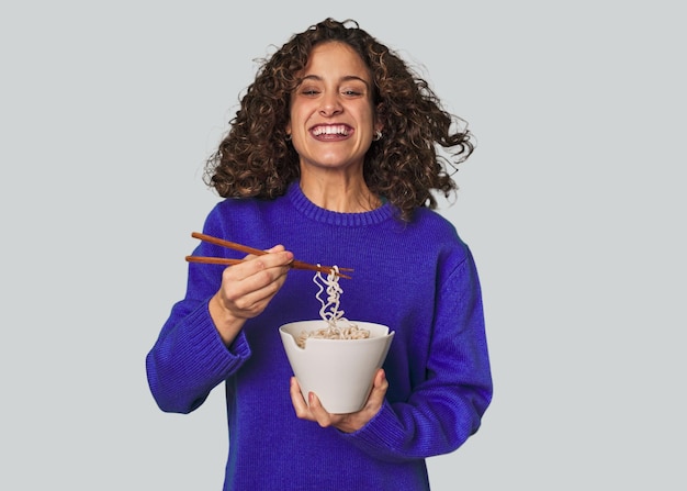 Foto uma jovem caucasiana comendo noddles com pauzinhos muito feliz