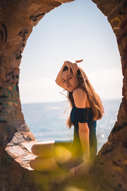 Uma jovem caucasiana ruiva sentada em um vestido azul à beira-mar