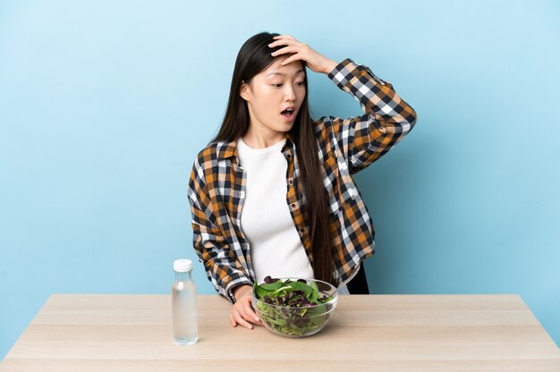 Uma jovem chinesa a comer uma salada a fazer um gesto de surpresa enquanto olha para o lado