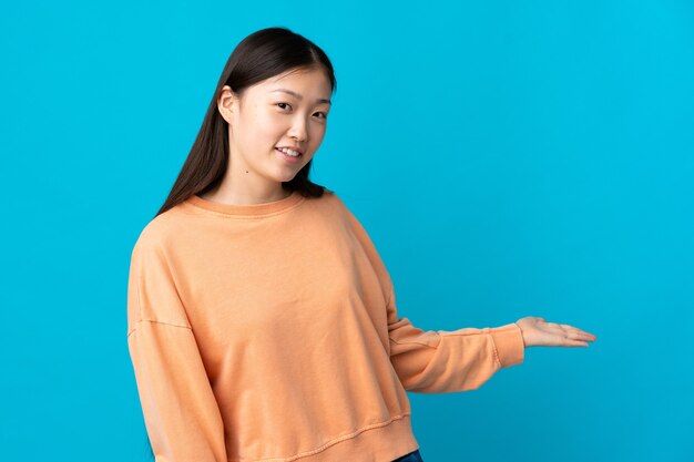 Uma jovem chinesa em um azul isolado estendendo as mãos para o lado para convidar para vir