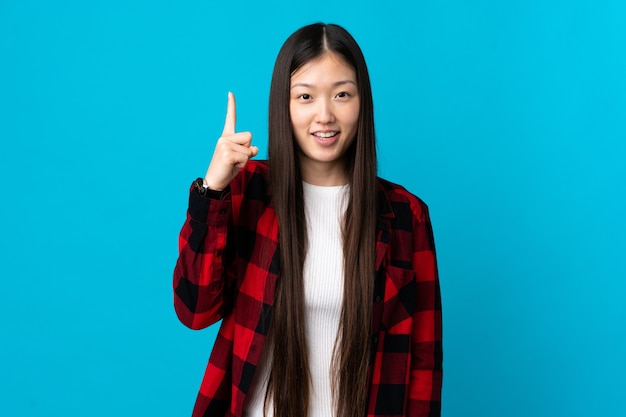 Uma jovem chinesa sobre uma parede azul isolada apontando para uma ótima ideia