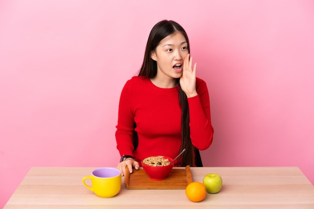 Uma jovem chinesa tomando café da manhã em uma mesa gritando com a boca bem aberta para o lado