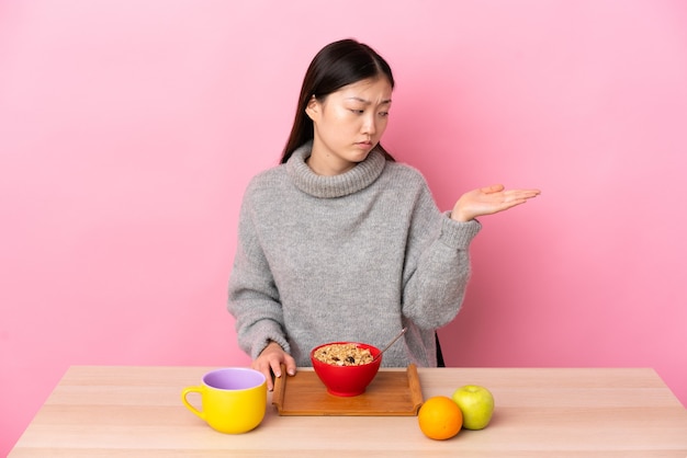 Uma jovem chinesa tomando café da manhã em uma mesa segurando copyspace com dúvidas